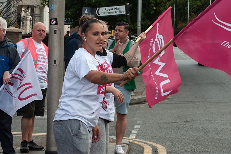 Trois personnes, dont deux agitant des drapeaux du syndicat CWU, sur une ligne de piquetage pendant les grèves du Royal Mail